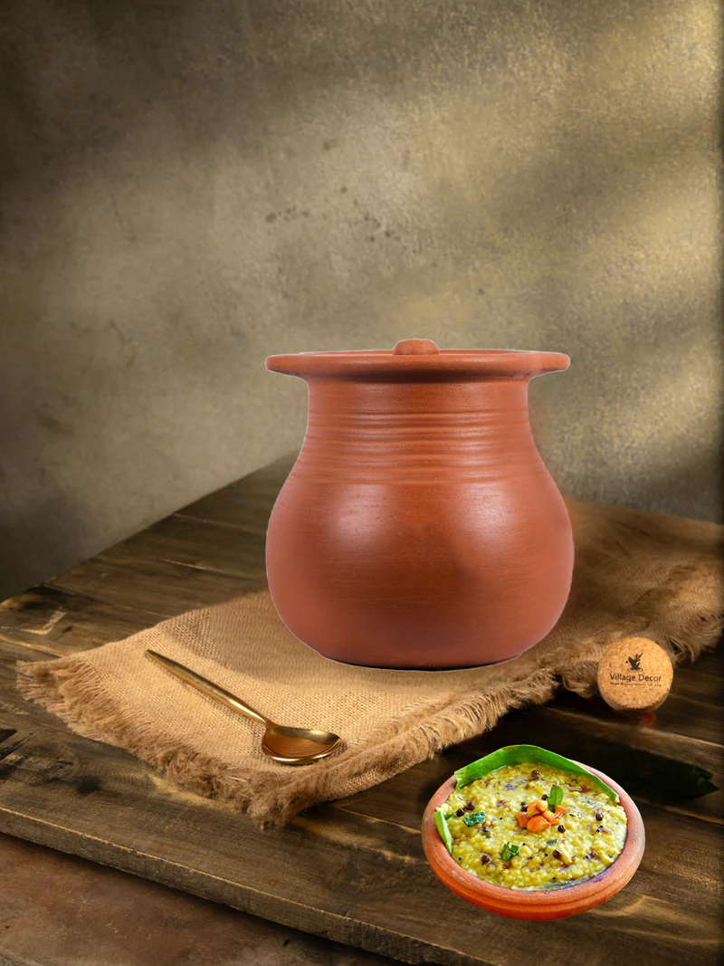 Earthen clay cooking pot with lid placed on a rustic wooden surface, accompanied by a brass spoon and a bowl of Pongal dish – perfect for healthy, traditional cooking.