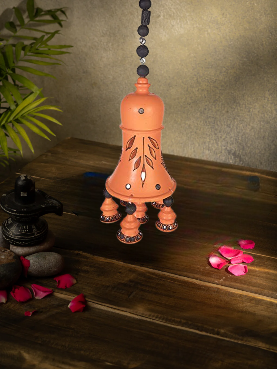 Handcrafted terracotta hanging bell with floral design, perfect for home decor, displayed with rose petals and sunflower background.