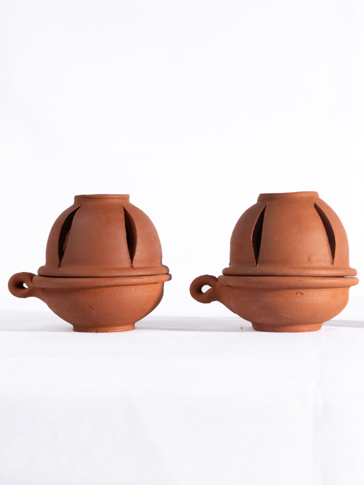 A pair of handcrafted terracotta oil diyas with lids, placed against a white background, ideal for pooja, spiritual use, and festive lighting.