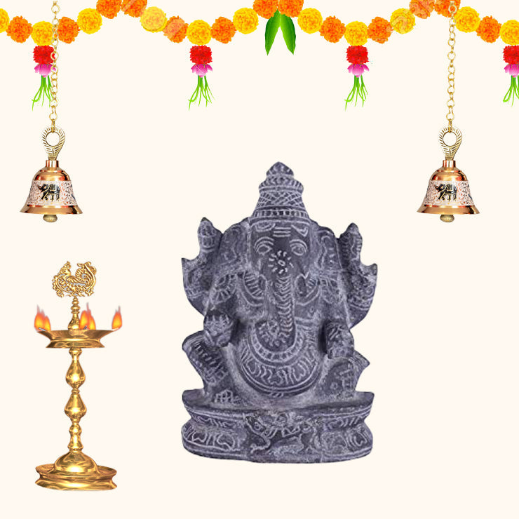 Black stone Ganesha idol with traditional pooja setup, festive home decoration with diya, bells and marigold flowers.