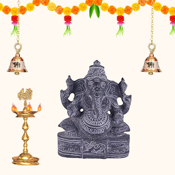 Black stone Ganesha idol with traditional pooja setup, festive home decoration with diya, bells and marigold flowers.