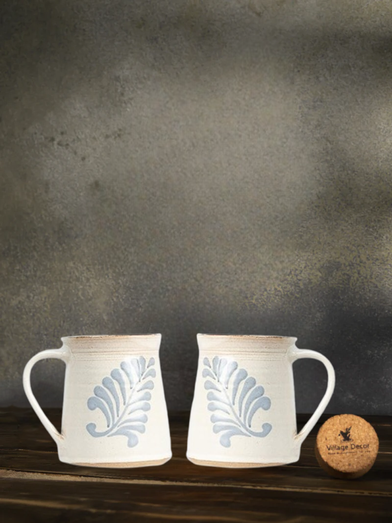 Two Ceramic Macaroon Cream White Color Mugs with blue leaf patterns on a wooden surface with a dark background.