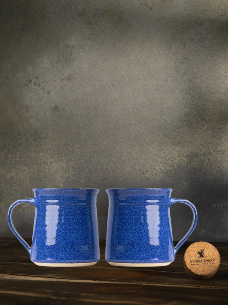 Two Navy blue Ceramic mugs on a wooden surface with a cork coaster and wooden block in the background.