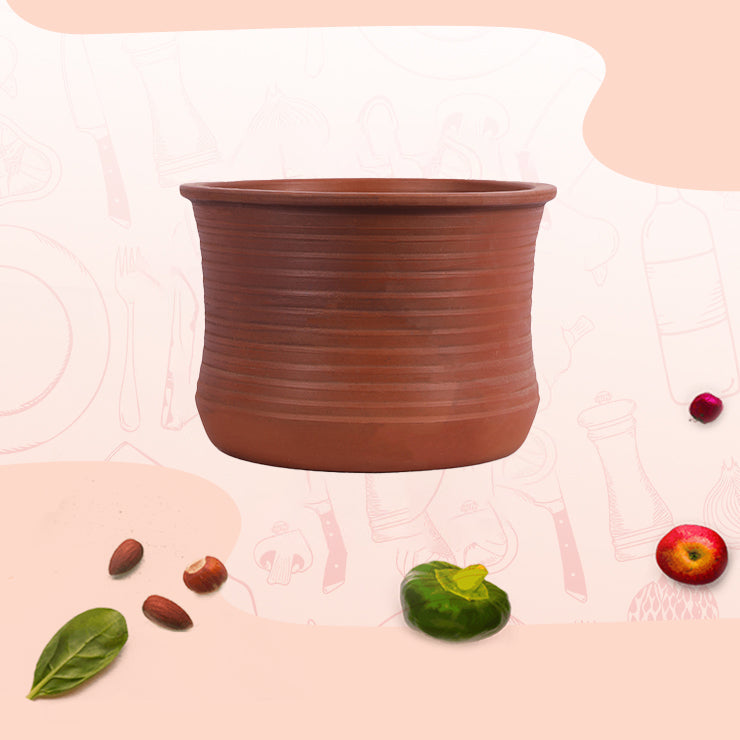 Traditional earthen clay Briyani pot surrounded by fresh ingredients like spinach, tomato, and nuts.
