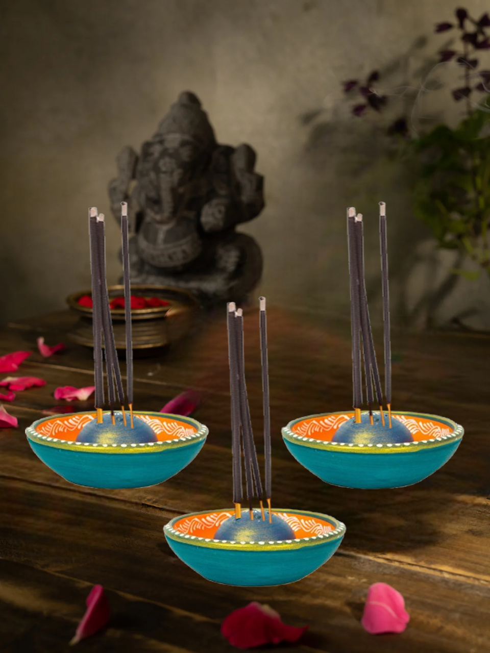 Colorful terracotta incense stick holders with agarbattis placed on a wooden table in a traditional puja setting with Ganesha idol in the background 