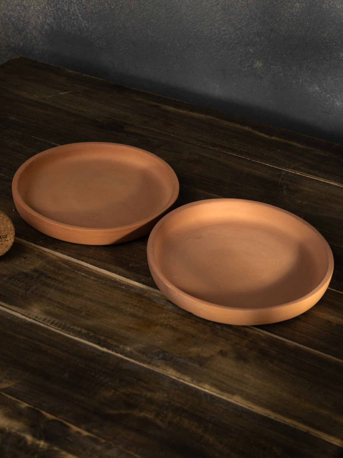 Two terracotta trays for flower pots placed on a wooden surface, perfect for collecting excess water and protecting indoor garden areas.

