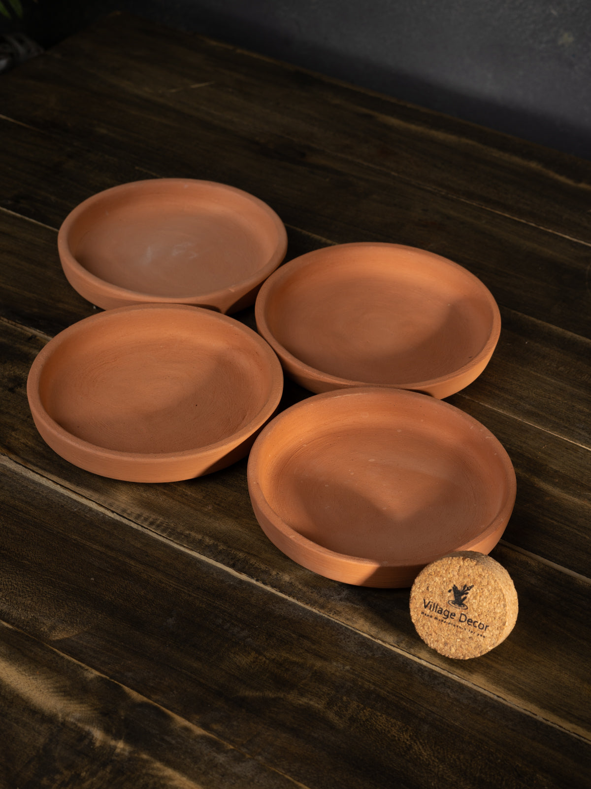 Four terracotta trays for flower pots placed on a wooden surface, perfect for collecting excess water and protecting indoor garden areas.
