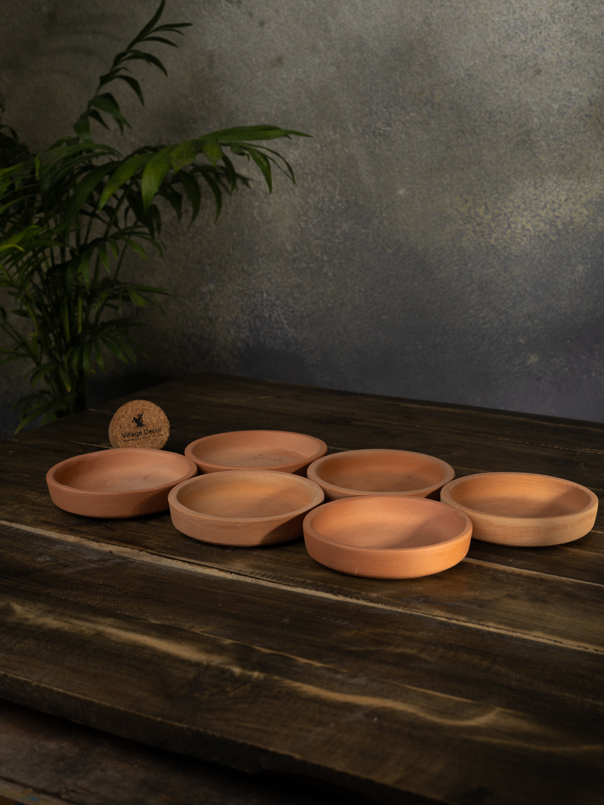 Four terracotta trays for flower pots placed on a wooden surface, perfect for collecting excess water and protecting indoor garden areas.
