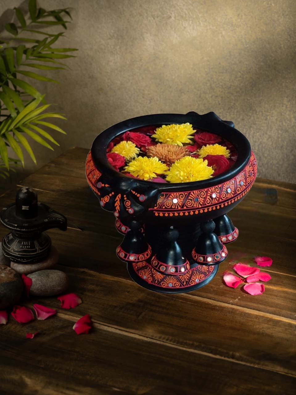 Handcrafted multicolor terracotta urli with floral design placed on a wooden surface, styled with rose petals and traditional decor for a festive look.
