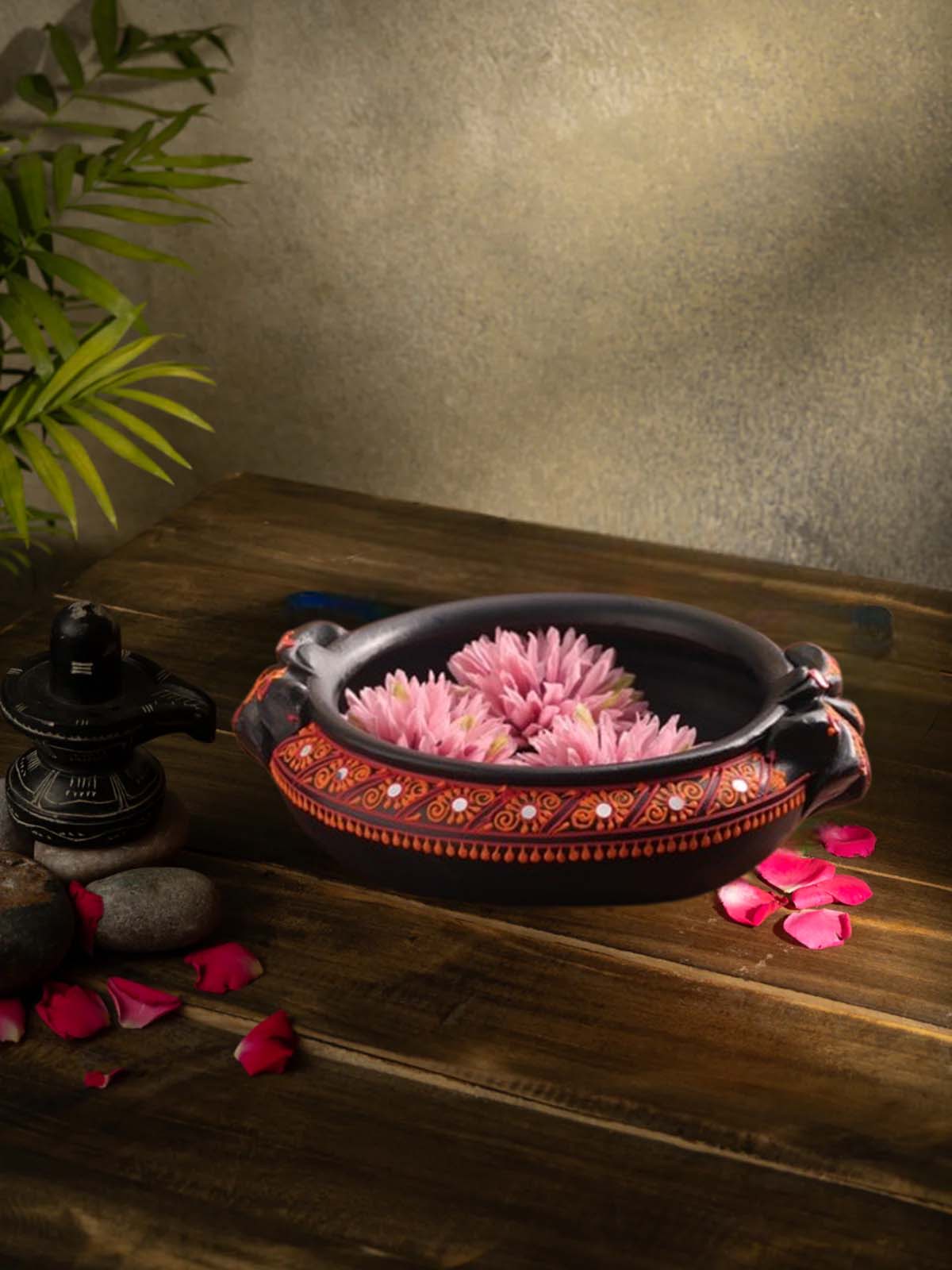 Handcrafted multicolor terracotta urli with floral design placed on a wooden surface, styled with rose petals and traditional decor for a festive look.
